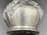a silver vase with a bird on it on a table