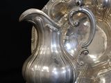 a silver plate and a silver pitcher on a black background