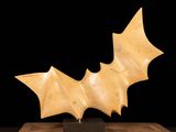sculpture of a bat on a wooden base against a black background