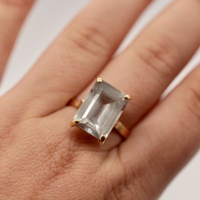 une image représentant la main d'une femme tenant une bague sertie d'une émeraude