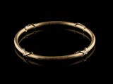 a gold bang bracelet with small beads on a black background