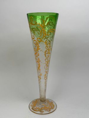 un vase en verre vert et or posé sur une surface blanche