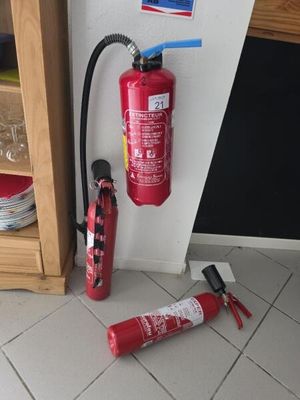 un extincteur posé à côté d'une lance à incendie, au sol